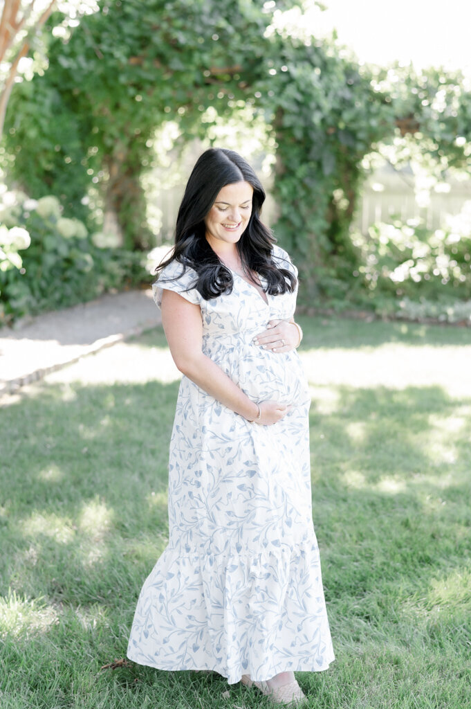pregnant woman stands in front of white hydrangeas 