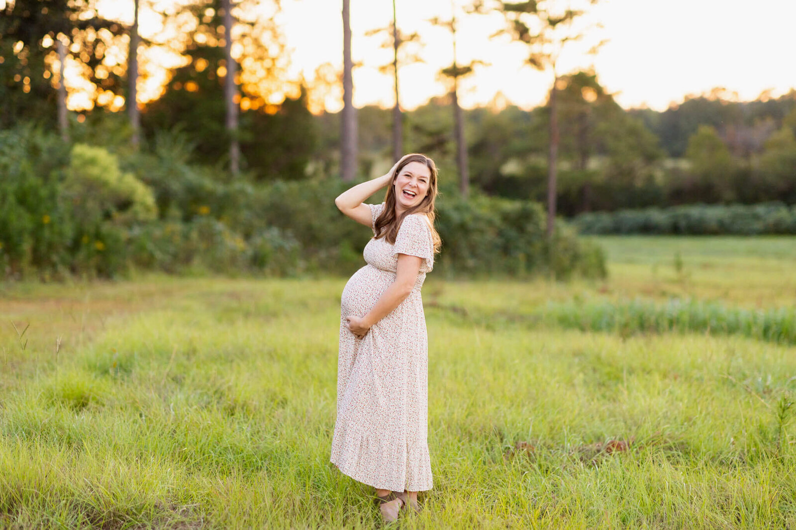 expectannt mother in a floral dress standing in a grassy field at golden hour