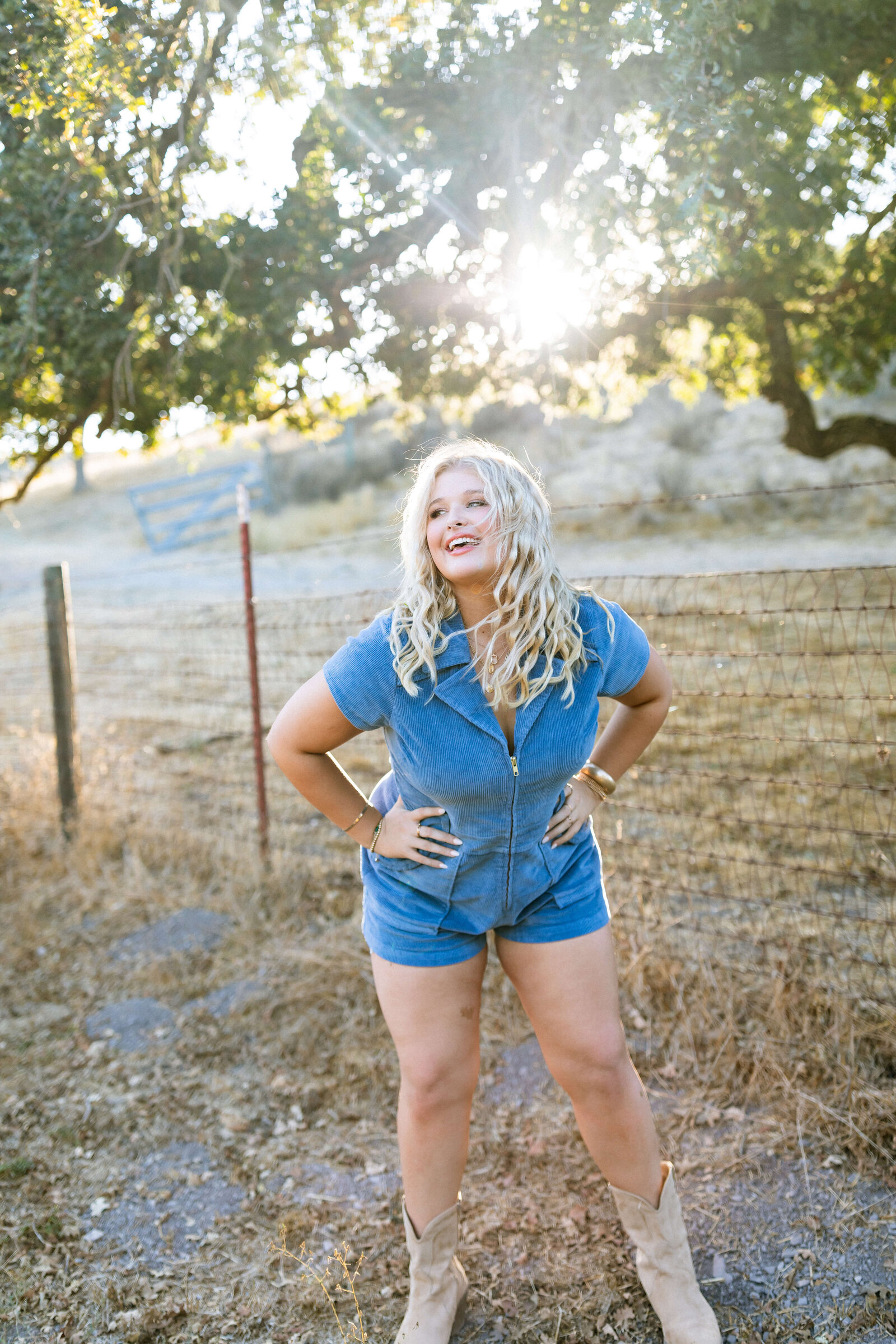 blonde girl wearing blue jean romper posing in a ranch