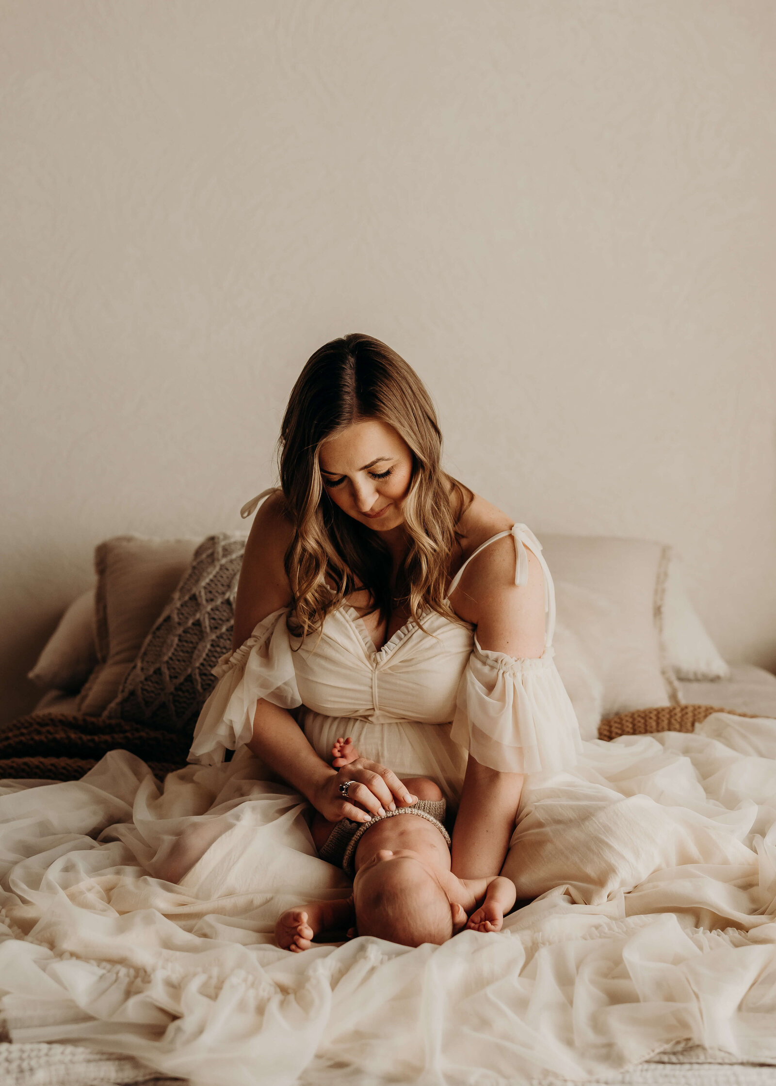 mother sits on bed wearing chiffon holding her newborn