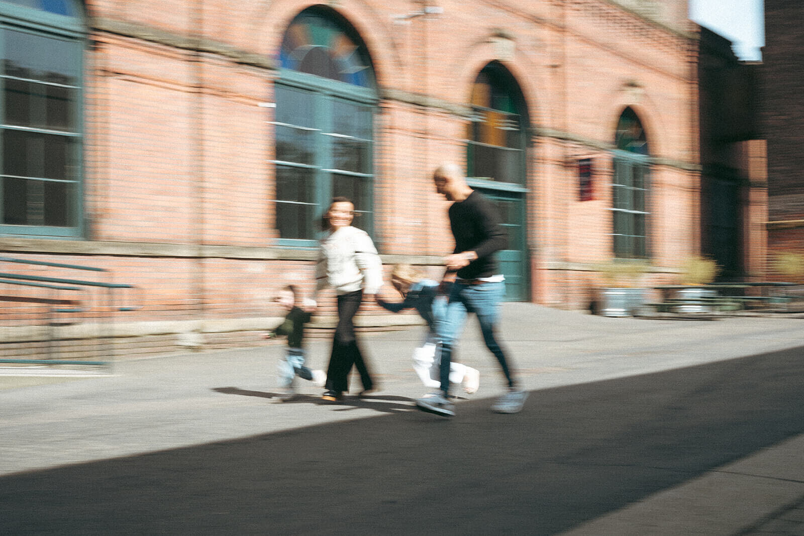 Playful candid of family running on city sidewalk with motion blur during documentary family photo session