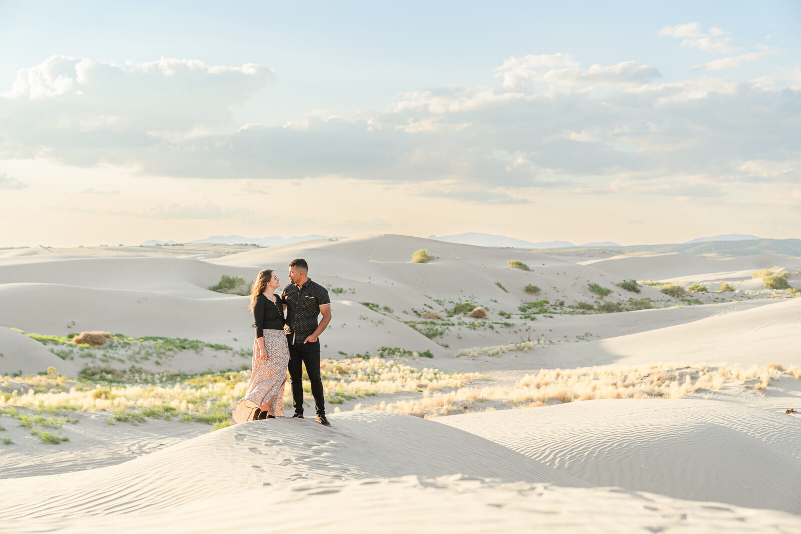 Utah engagement photography of an engaged couple gazing at each other while standing on a sand dune at Little Sahara, Nephi