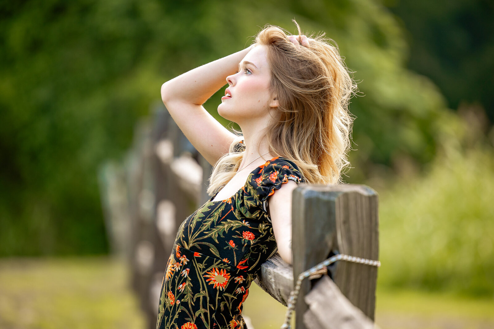 senior girl leaning against a fence in faust park with hand brushing through hair