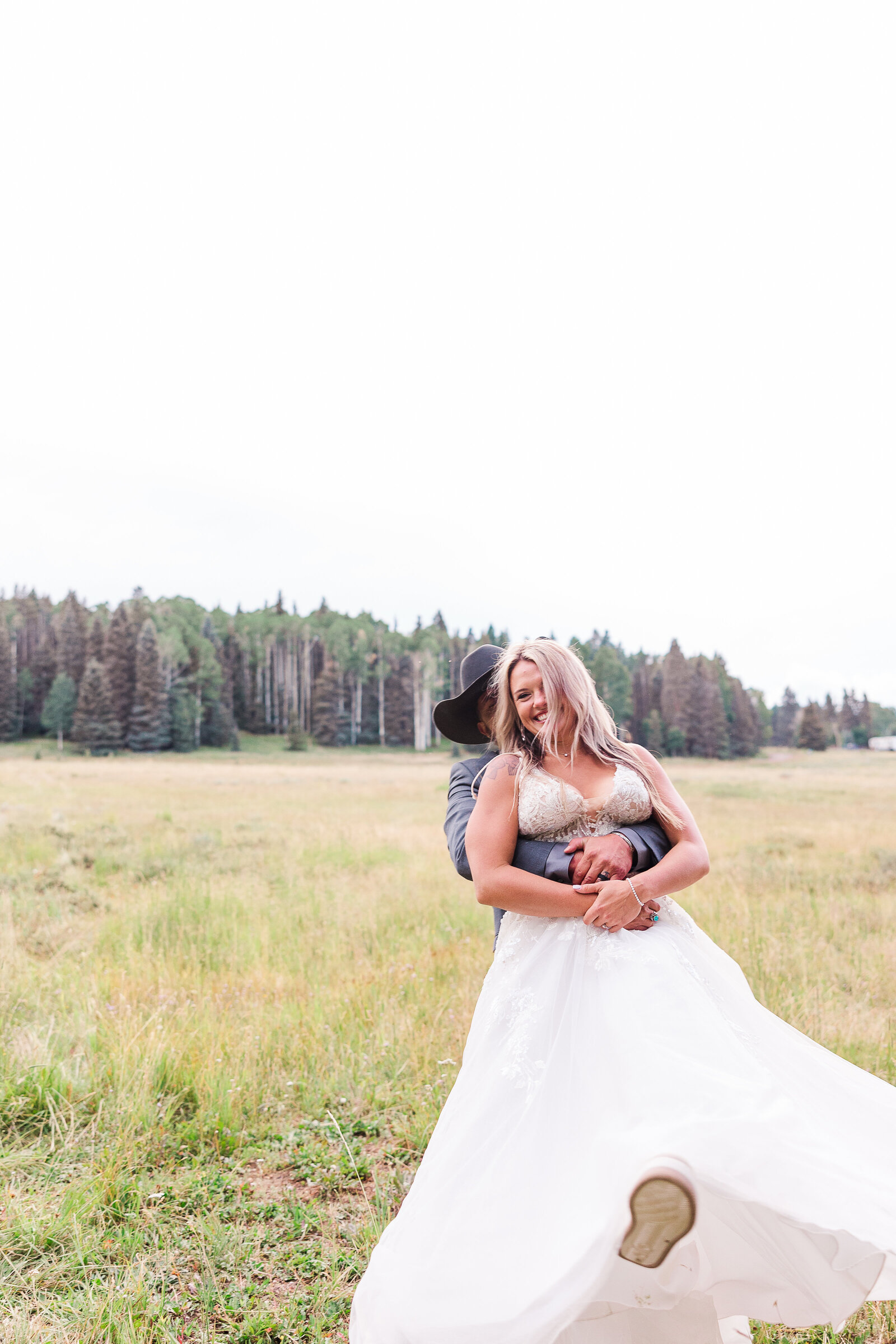 Groom holds bride around the waist as he spins her and they laugh together