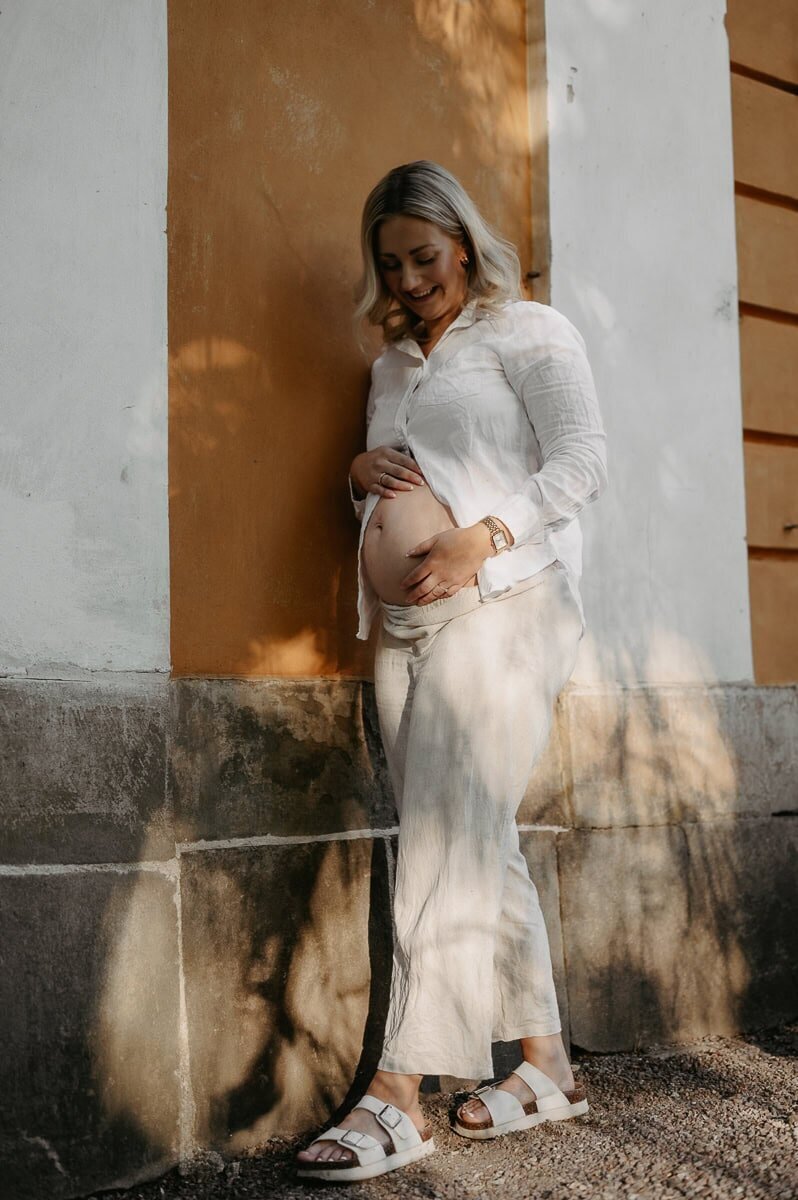 Gravid kvinna står framför orange fin vägg, håller om sin gravida mage.