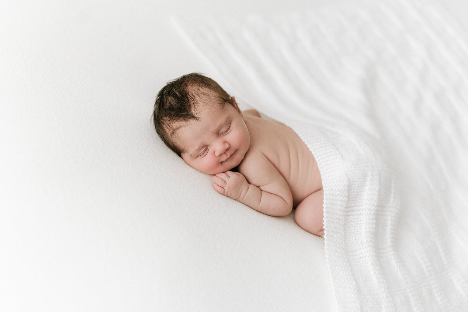 Baby sleeps on a white beanbag in the photography studio