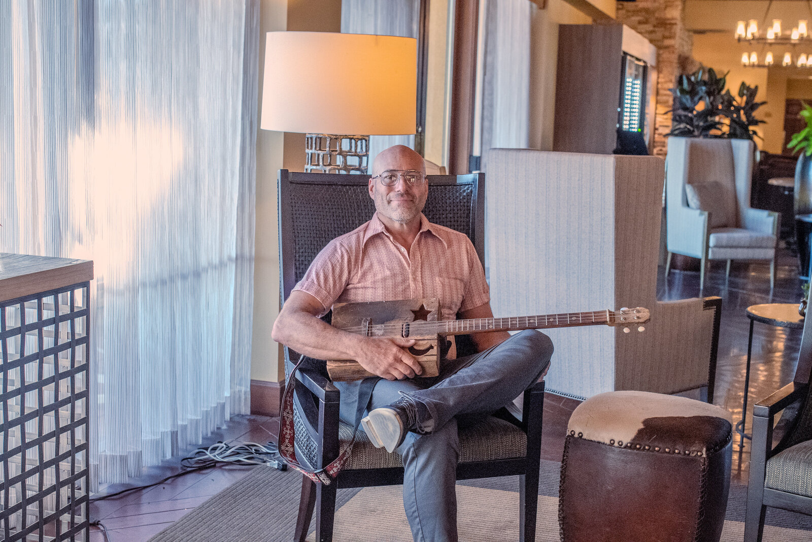 Smiling man sitting in a modern chair holding a guitar in a warmly lit room, photographed by Vyrl Photo, showcasing business photography Tucson.