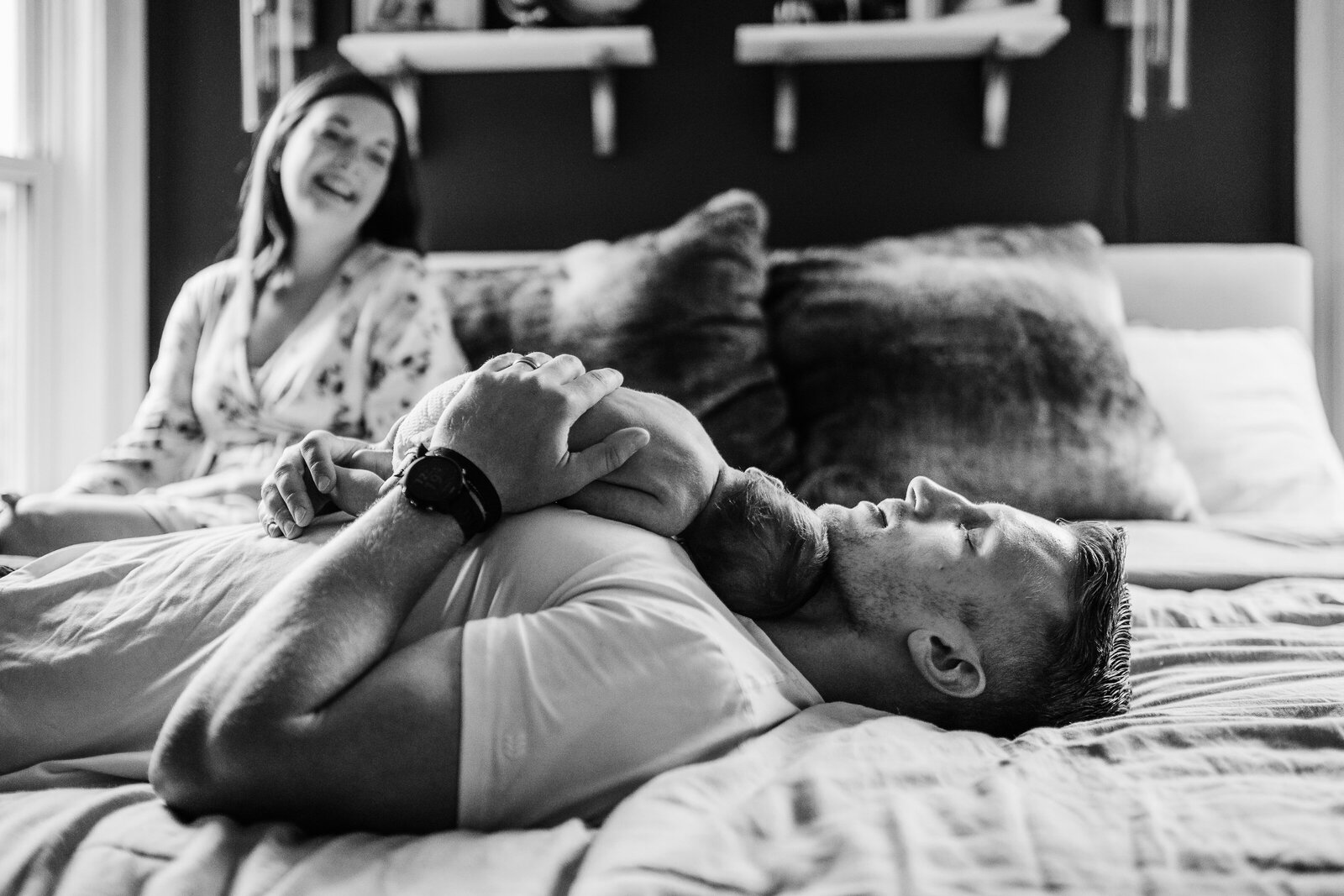 black and white image of dad laying on bed cradling newborn to chest