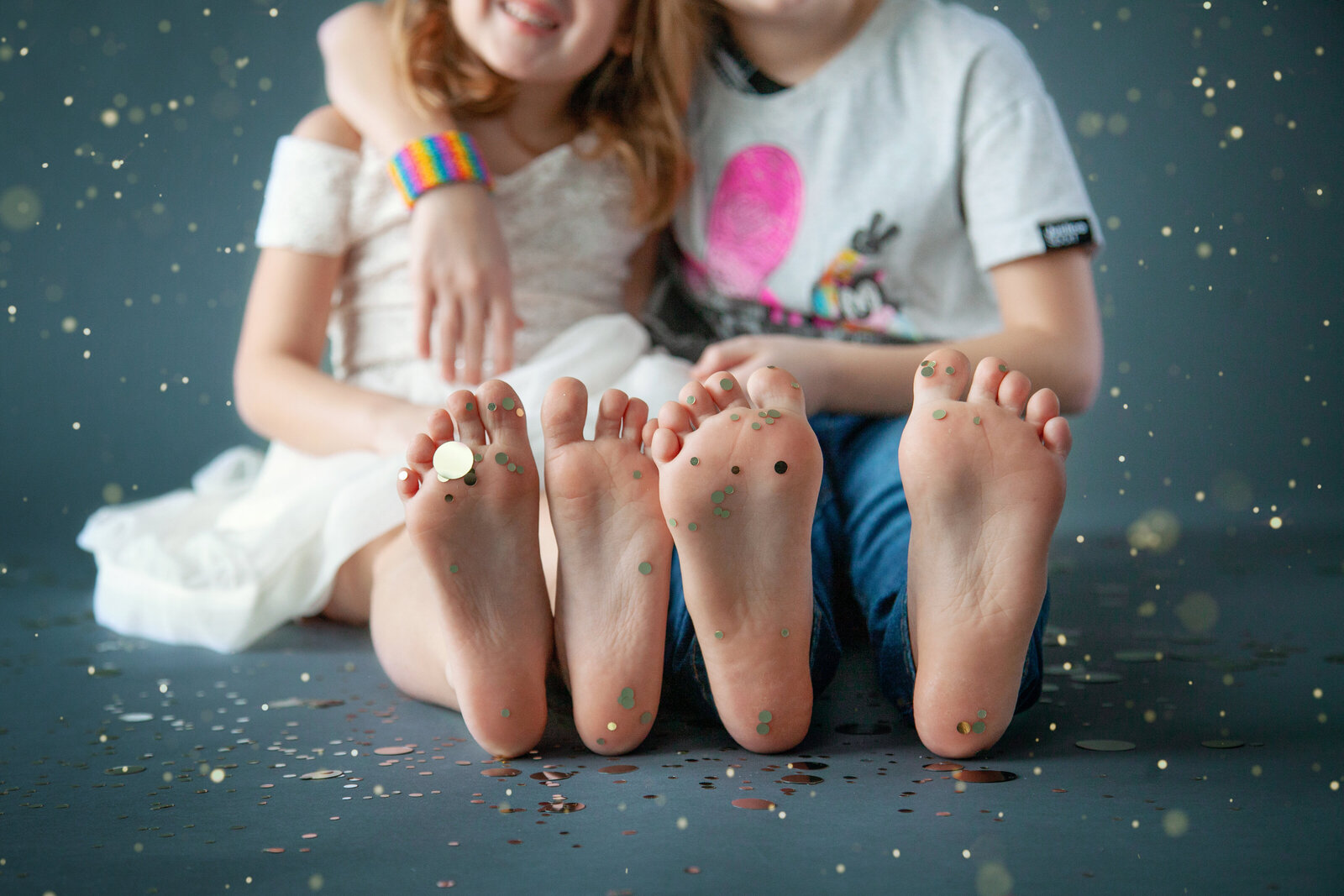 Sisters sitting close, focused on bottoms of their feet covered in glitter.
