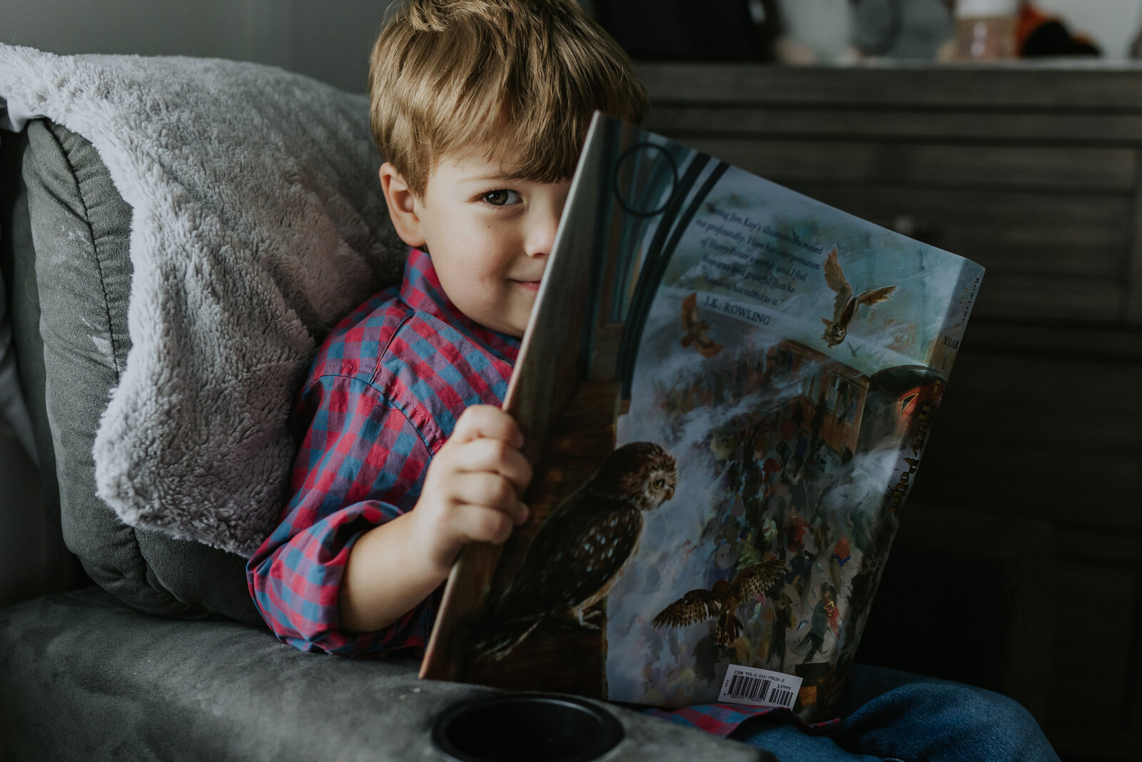 A young boy reads Harry Potter and peaks at the camera