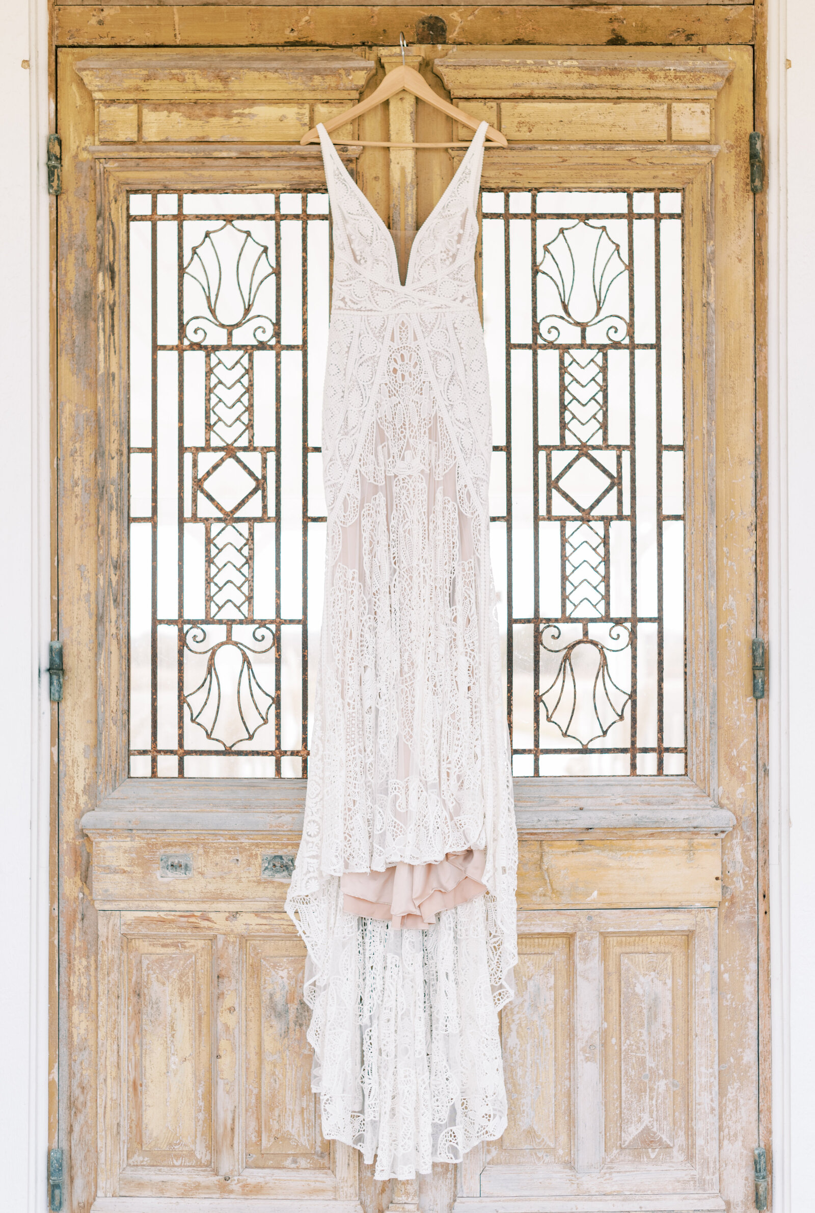 Portrait of a cream lace wedding gown hanging on a distressed wooden door