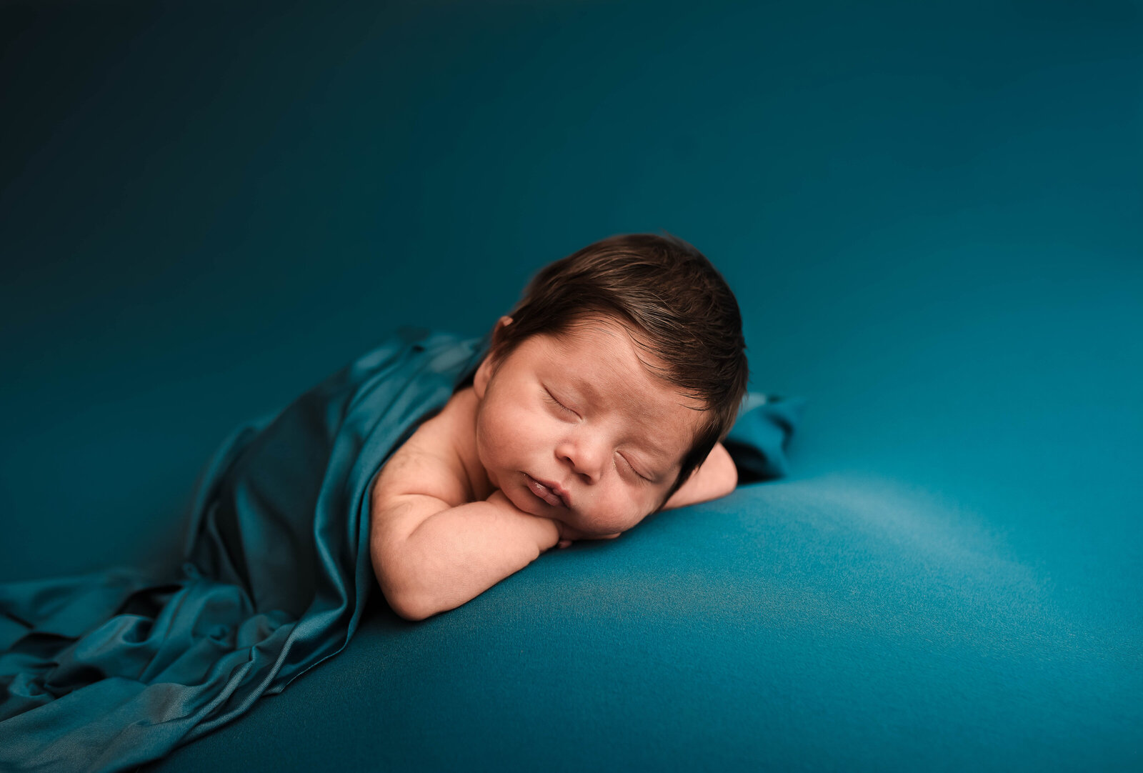 newborn baby laying on stomach covered in blue silk blanket