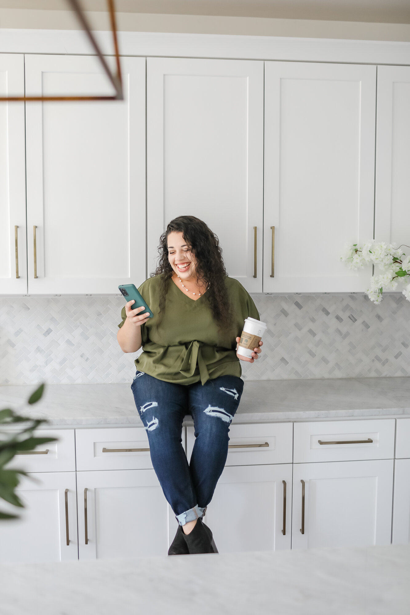 color image of  VA sitting on counter with her cell phone and coffee