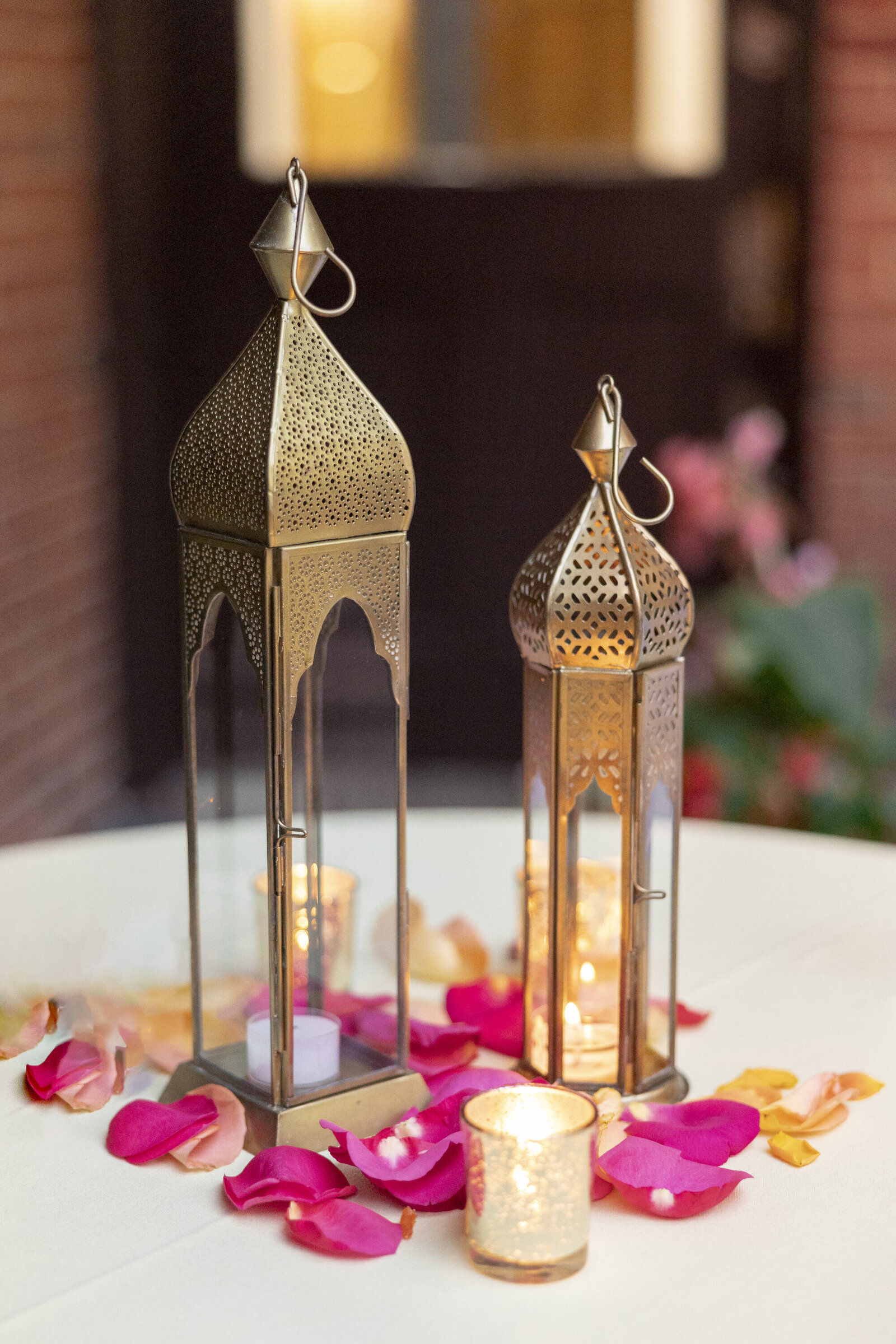 Ornate gold lanterns on a cocktail table with pink and orange rose petals scattered around them.