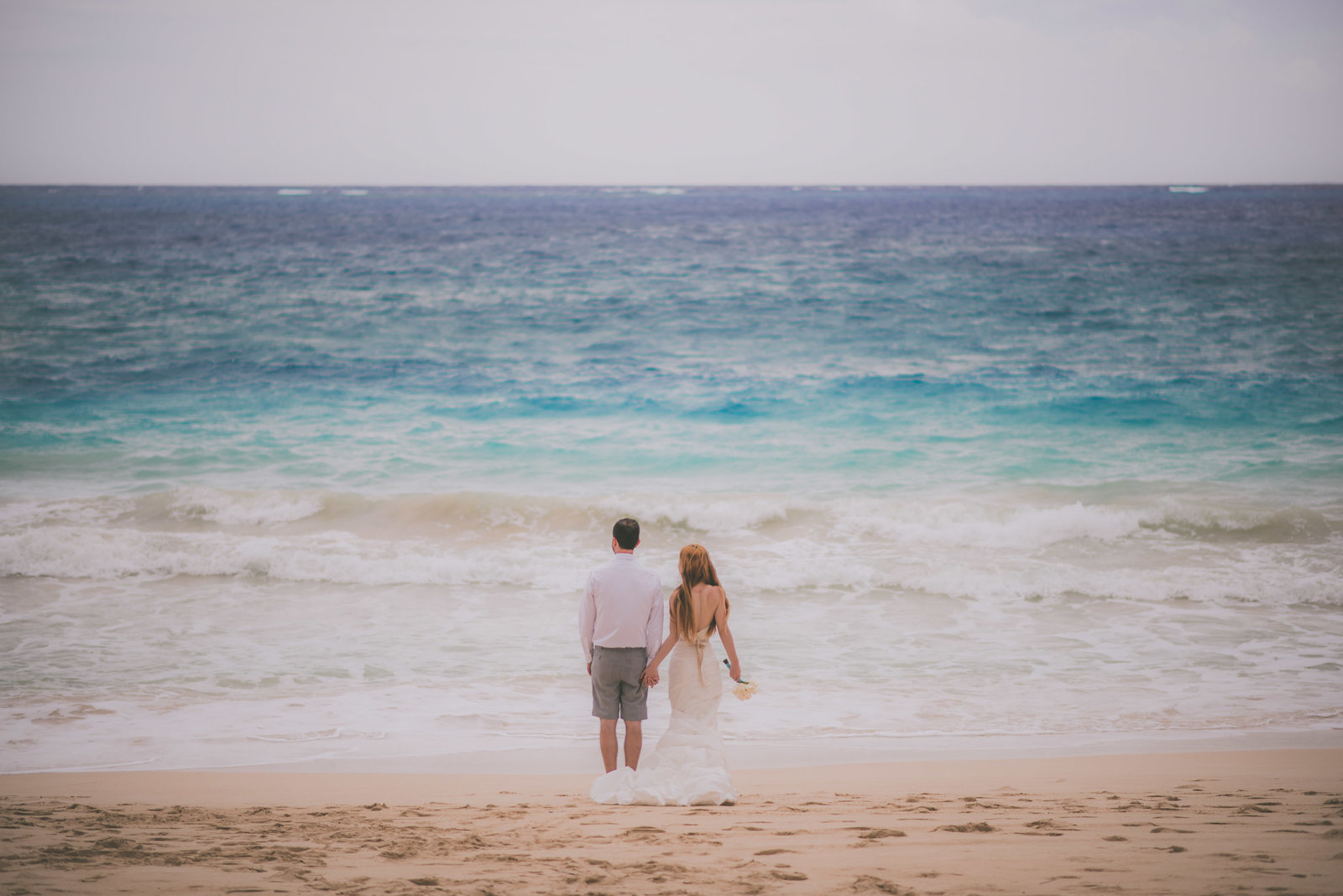 Bride and groom facing the ocean in Hawaii.