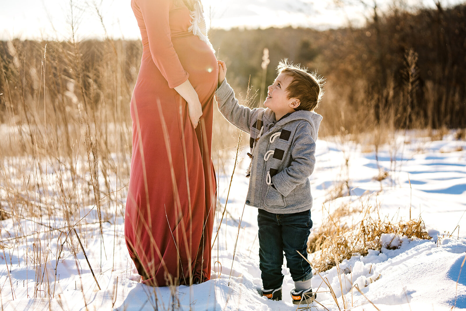 toddler boy touches pregnant moms belly in snowy field
