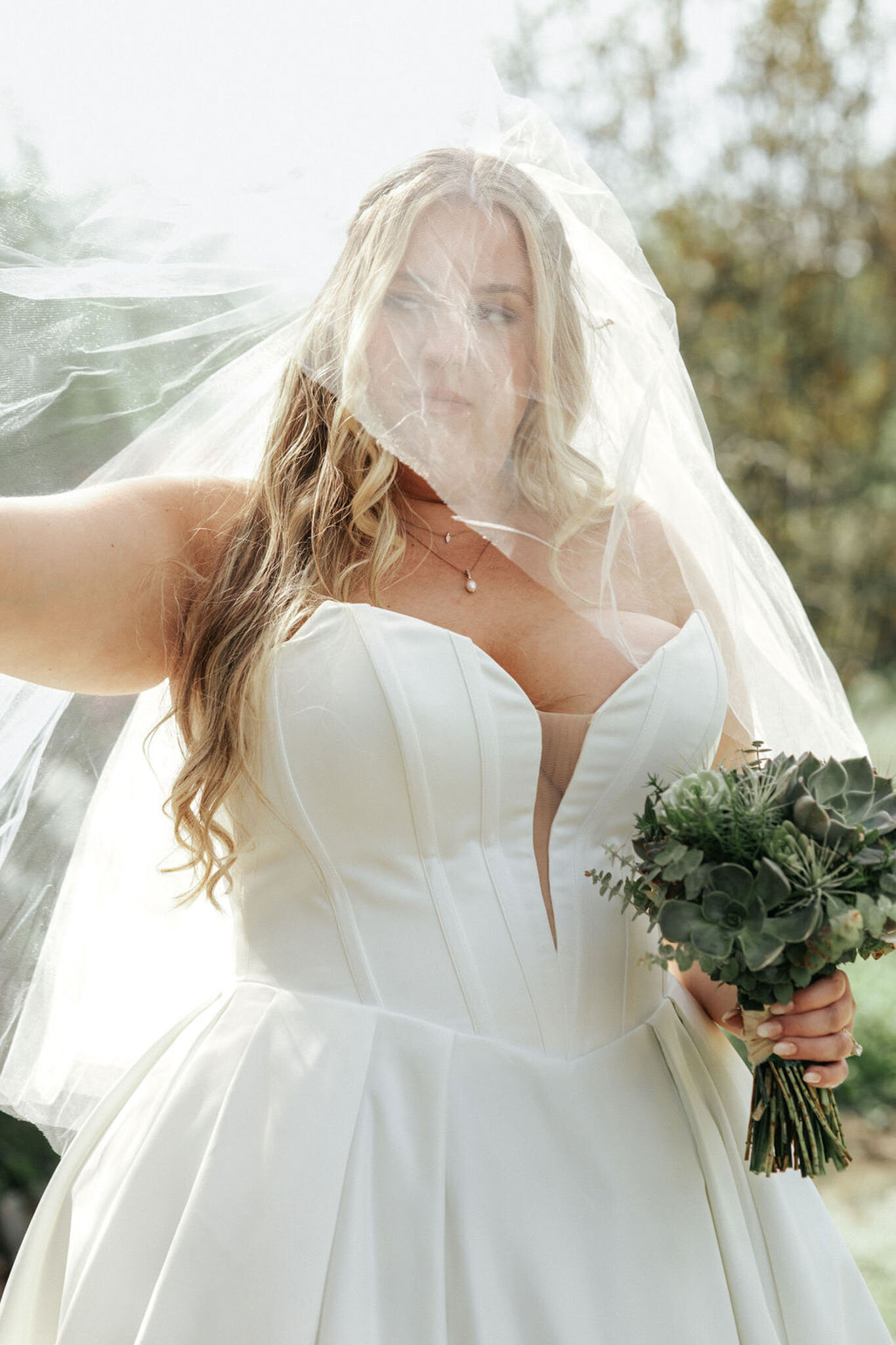 Bride insider her veil holding a floral bouquet