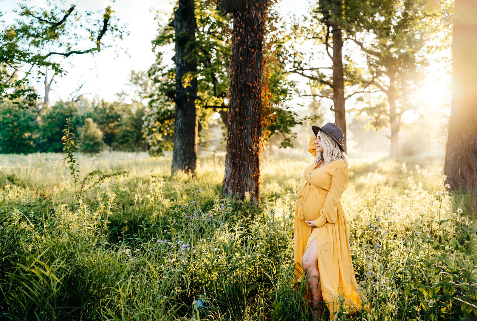 pregannt mom wearing a hat posng  in wooded field at sunrise
