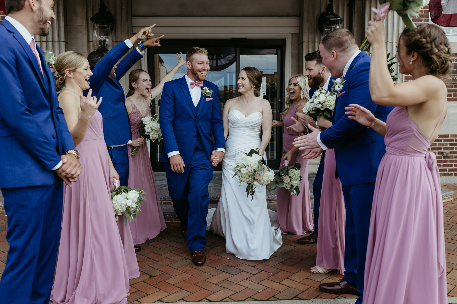 A bride and groom walk between their wedding party while laughing