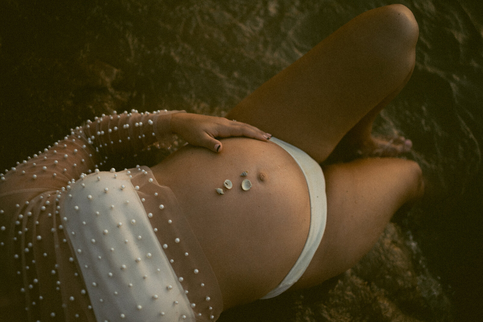 A detail shot during a seaside maternity session with seashells on her pregnant belly.