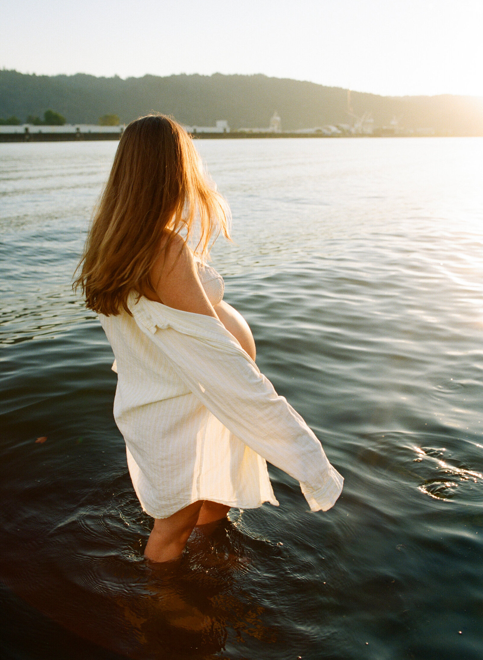 Pregnant mother partially in the Williamette River at golden hour in Portland, Oregon.