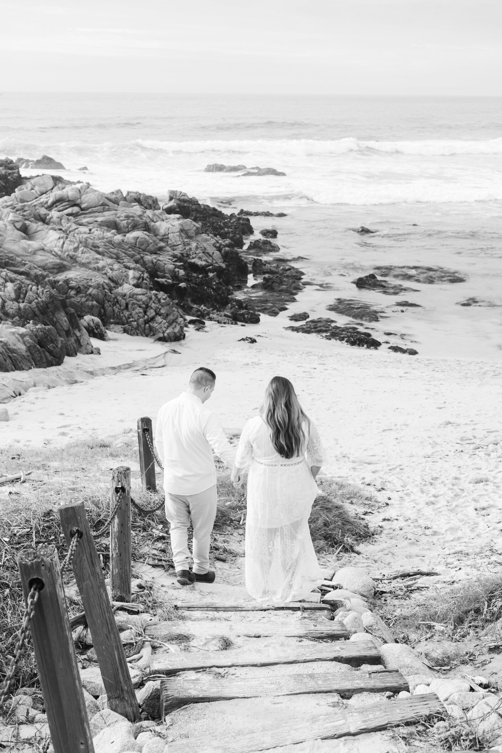 An engaged man and woman take photos on the beach in Pacific Grove, Monterey, California near Big Sur.