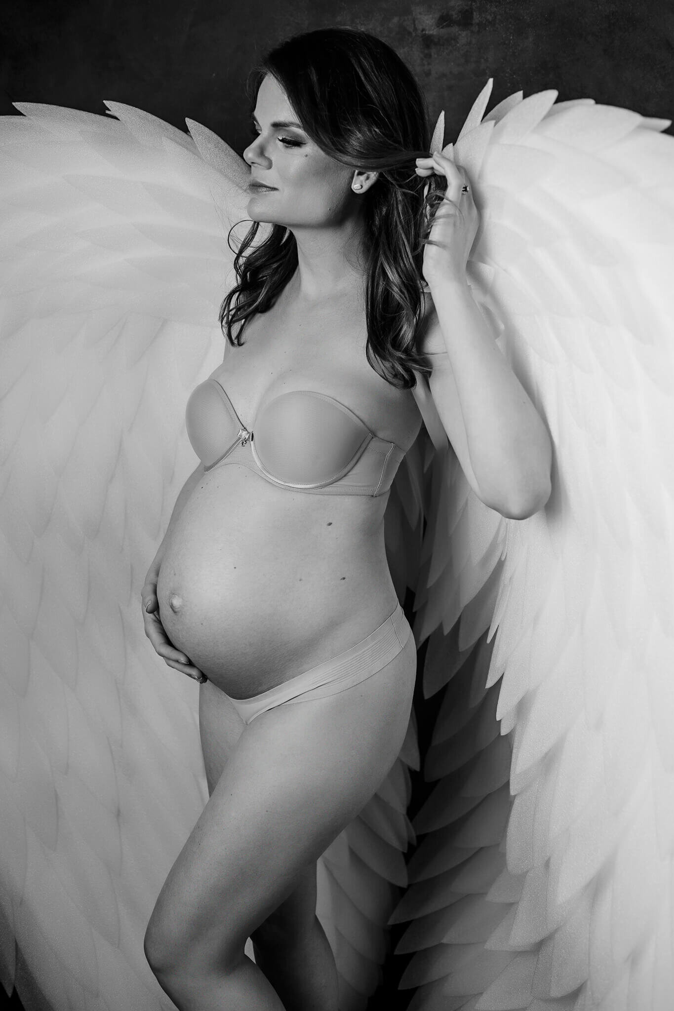 Maternity photo in black and white, she is wearing white wings which makes a romantic mom to be picture