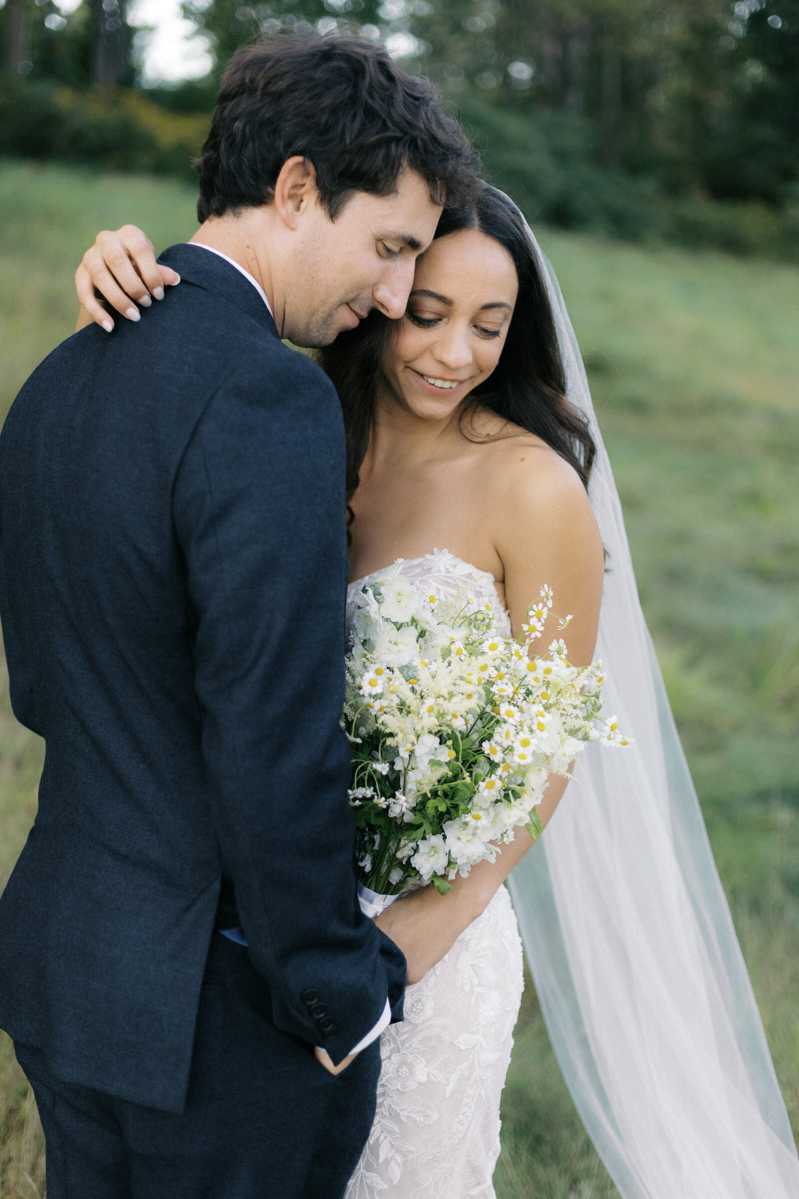 bride and groom hugging at their vermont wedding. bride is holding a simple green and white floral bouquet