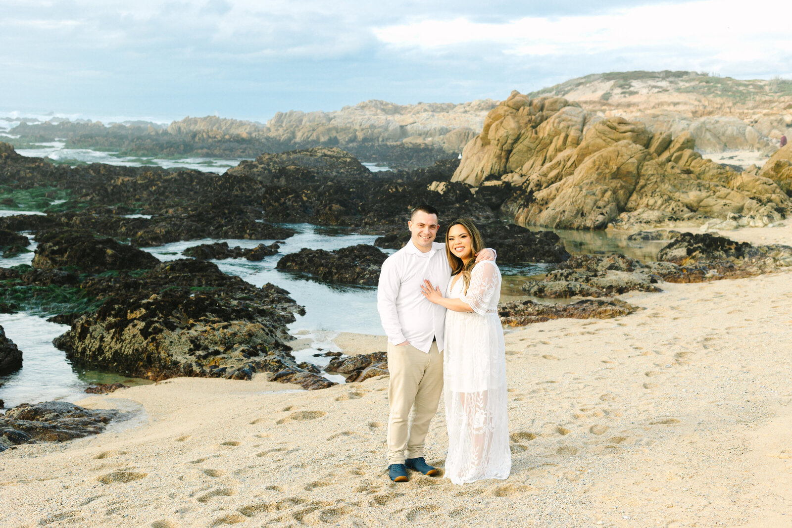 An engaged man and woman take photos on the beach in Pacific Grove, Monterey, California near Big Sur.
