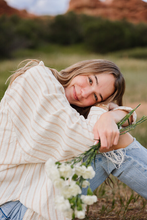 Girl puts head on knees while holding flowers.