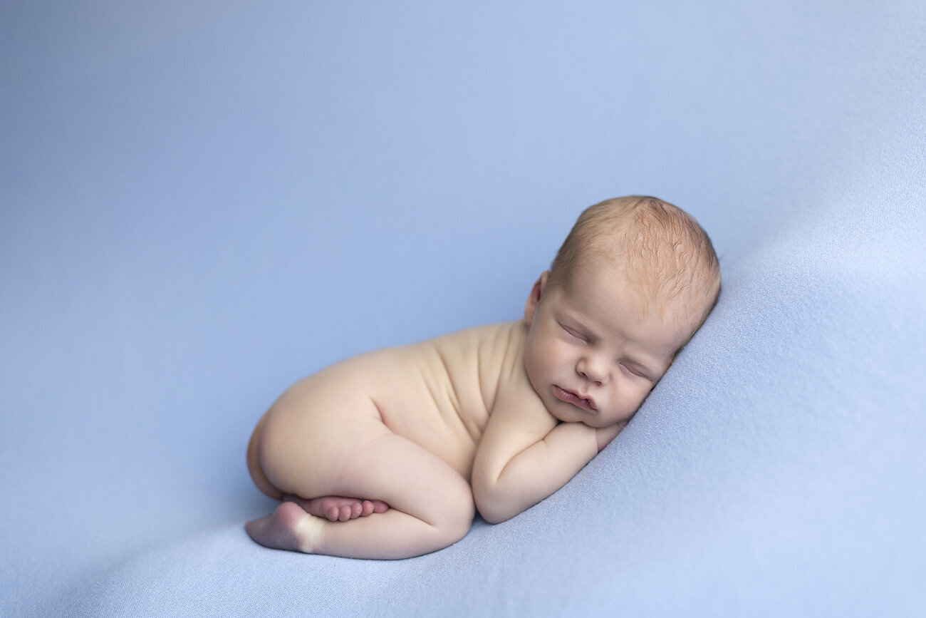Newborn boy sleeping on blue fabric.