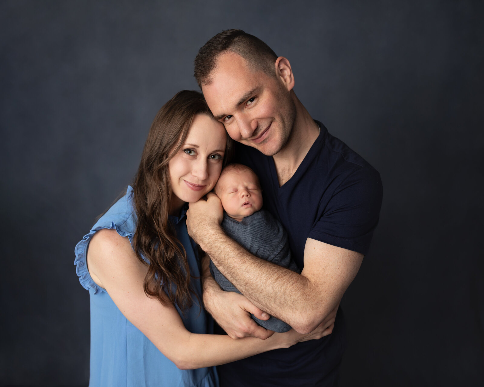 mom and dad holding newborn baby boy wrapped in blue for newborn studio portraits