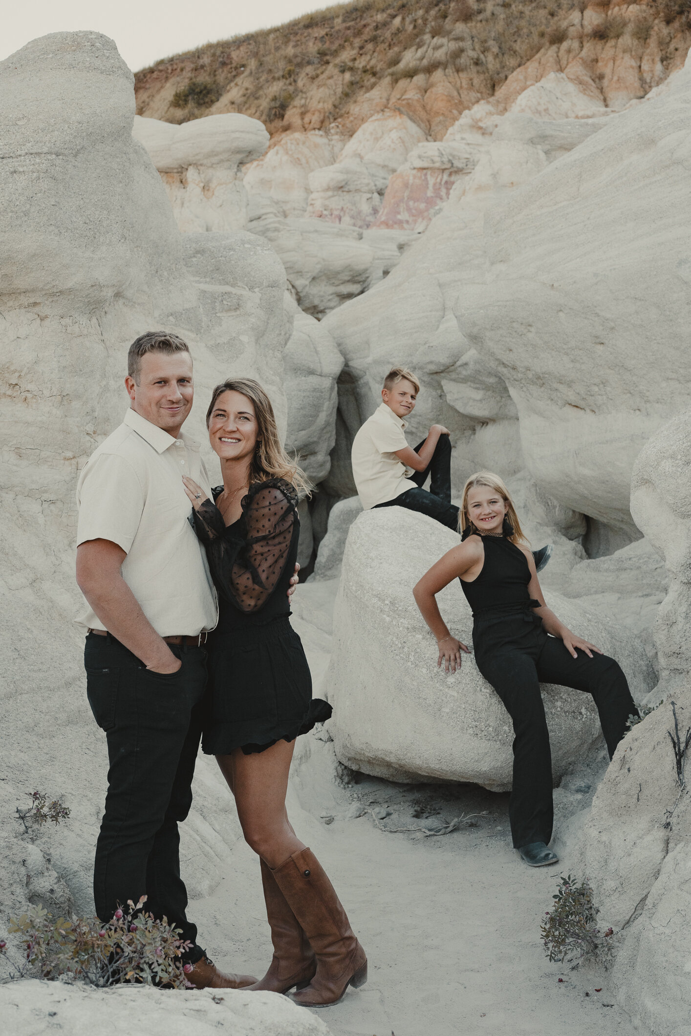 A husband and wife and their two children all dressed in black and white pose with the backdrop of Sandstone at the unique location of the Colorado paint mines in Calhan, Colorado.