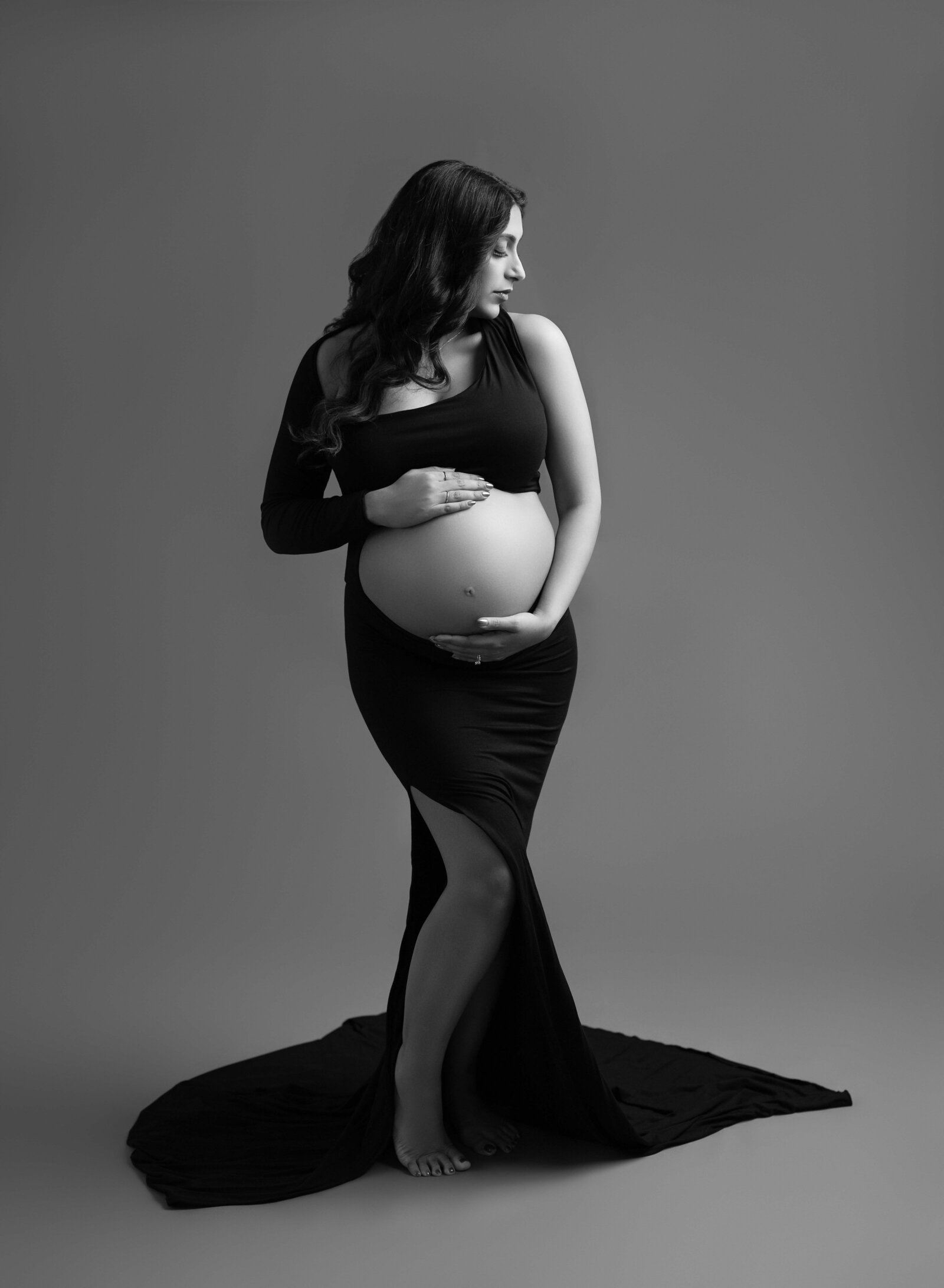 B&W photo of Mom dressed in sleek maternity dress holding baby bump. Photo taken at Luxury Maternity photo studio in Atlanta, GA.