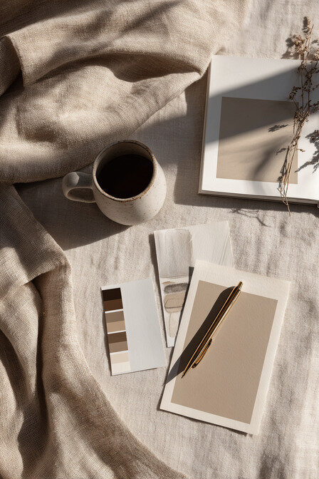 Editorial flatlay featuring a ceramic coffee cup, color palette cards, and a design notebook on soft linen fabric, illustrating Kathalyst Design Studio’s refined and natural brand style.