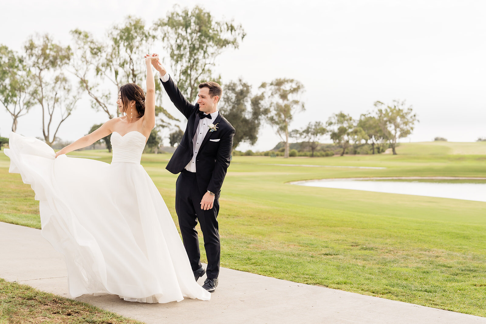 A groom twirling his bride on a side walk with a golf course in the background at The Lodge at Torrey Pines