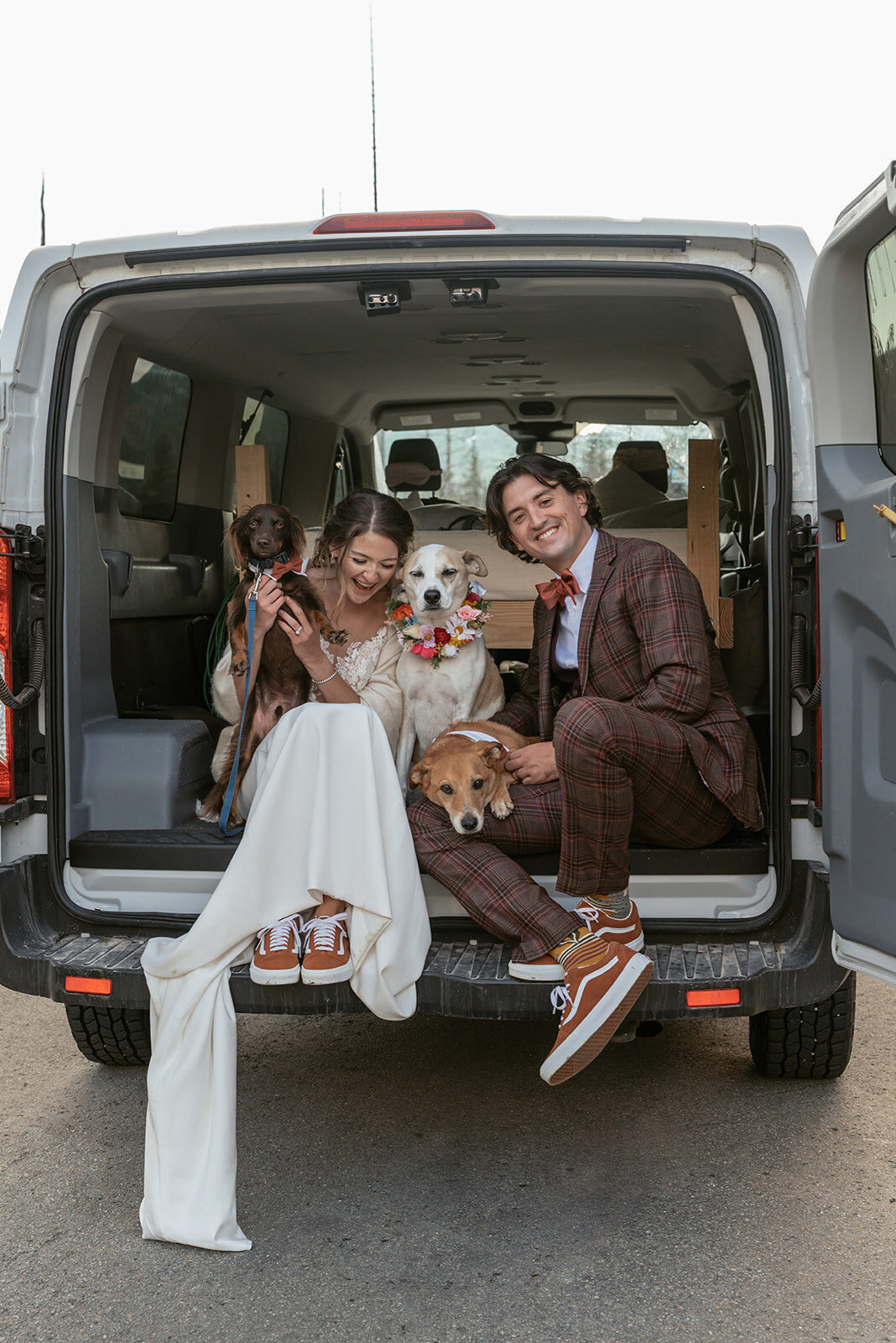 A newlywed couple sits in the back of their adventure van with their four dogs, all dressed up for the wedding day, after their Glacier National Park elopement, captured by Sydney Breann Photography.