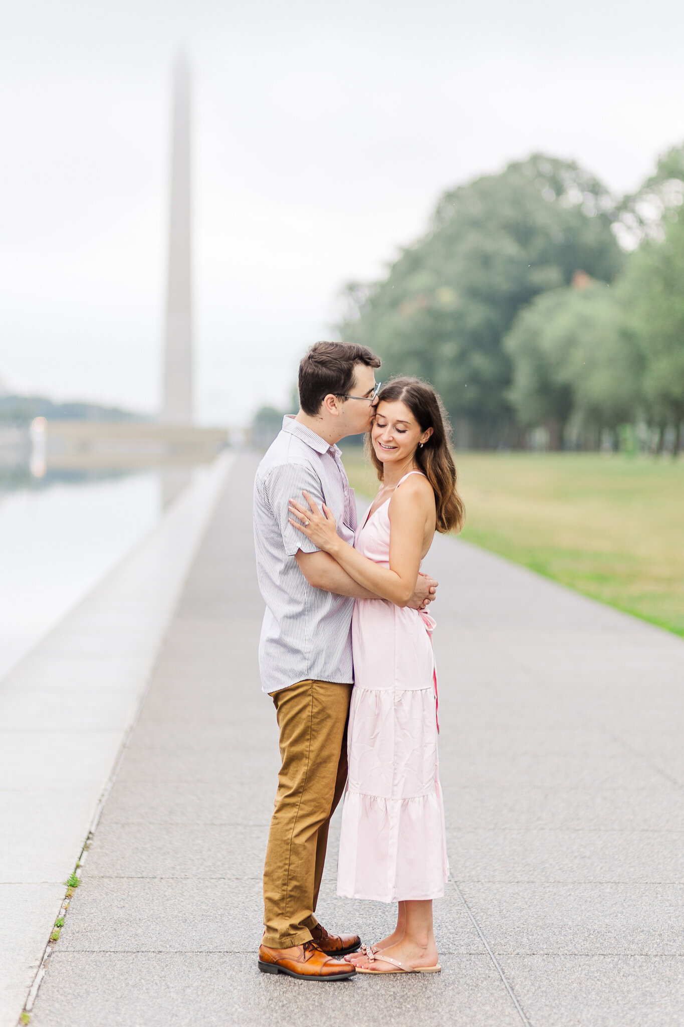 A man kisses his fiance on the temple with the Washington Monument in the background