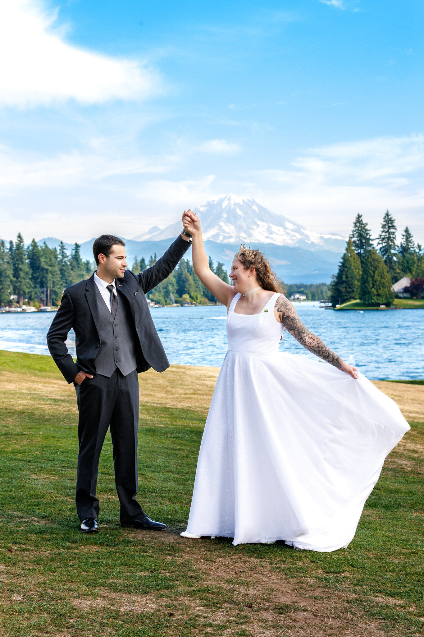 Romantic Seattle wedding portrait of a bride and groom dancing outdoors on a beautiful sunny day. Mount Rainier rises in the distance, and the sunlight reflects off the water behind them, creating a soft, glowing backdrop.