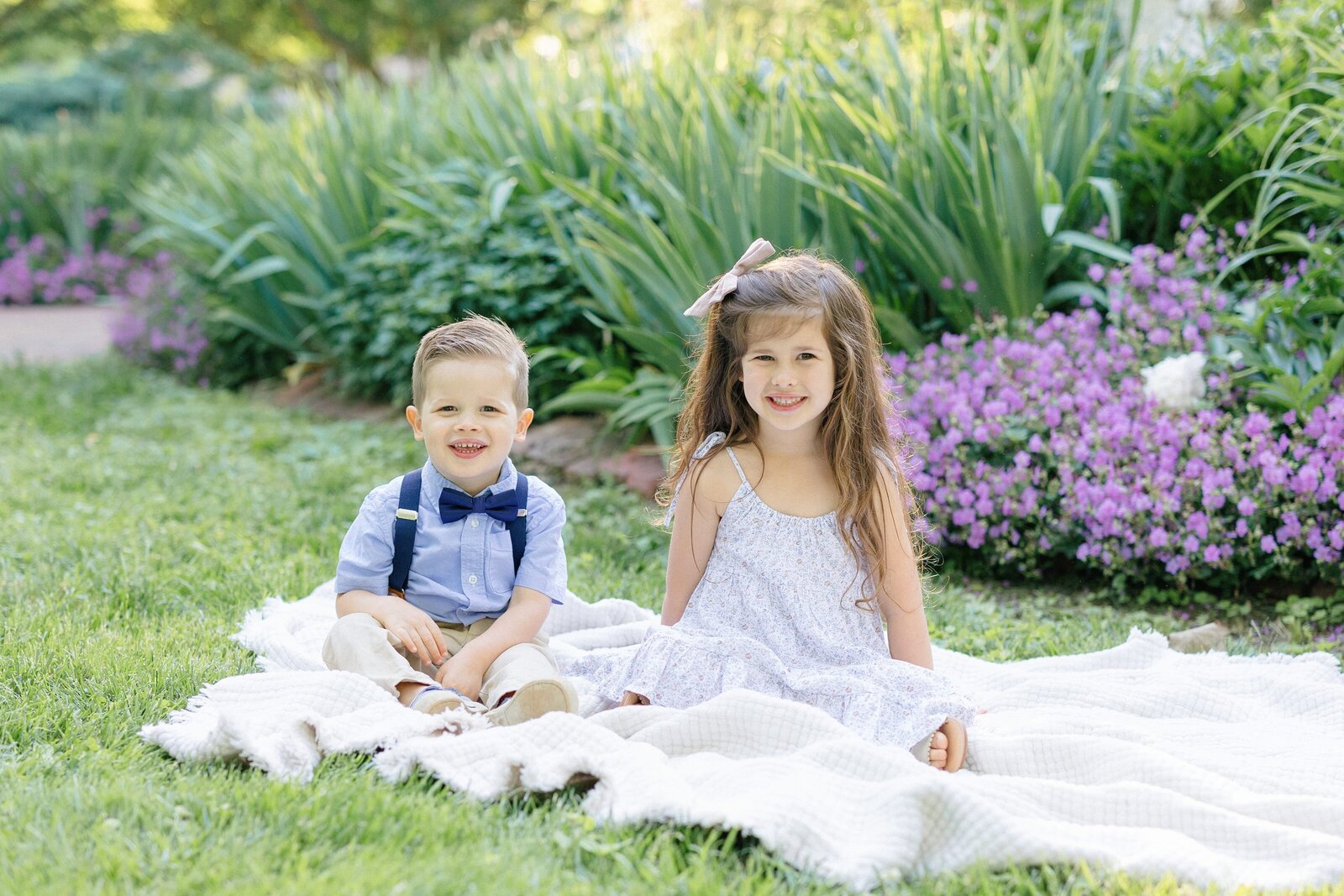 Brother and sister sitting on a white quilt in a garden during their louisville family photography session