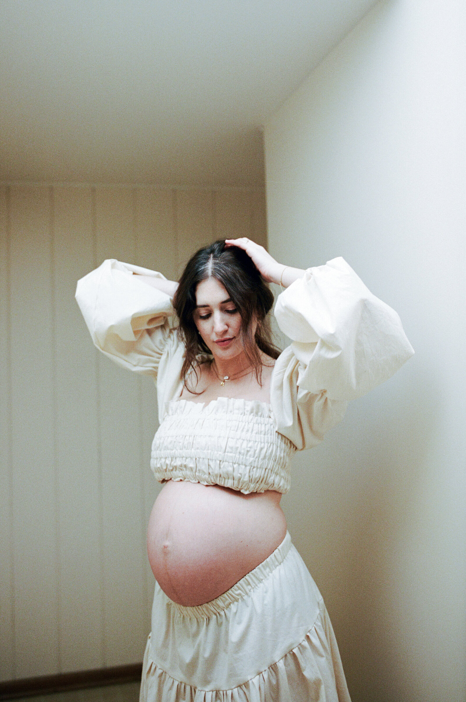 Pregnant mother in all white adjusting her ponytail in her Portland, Oregon home.