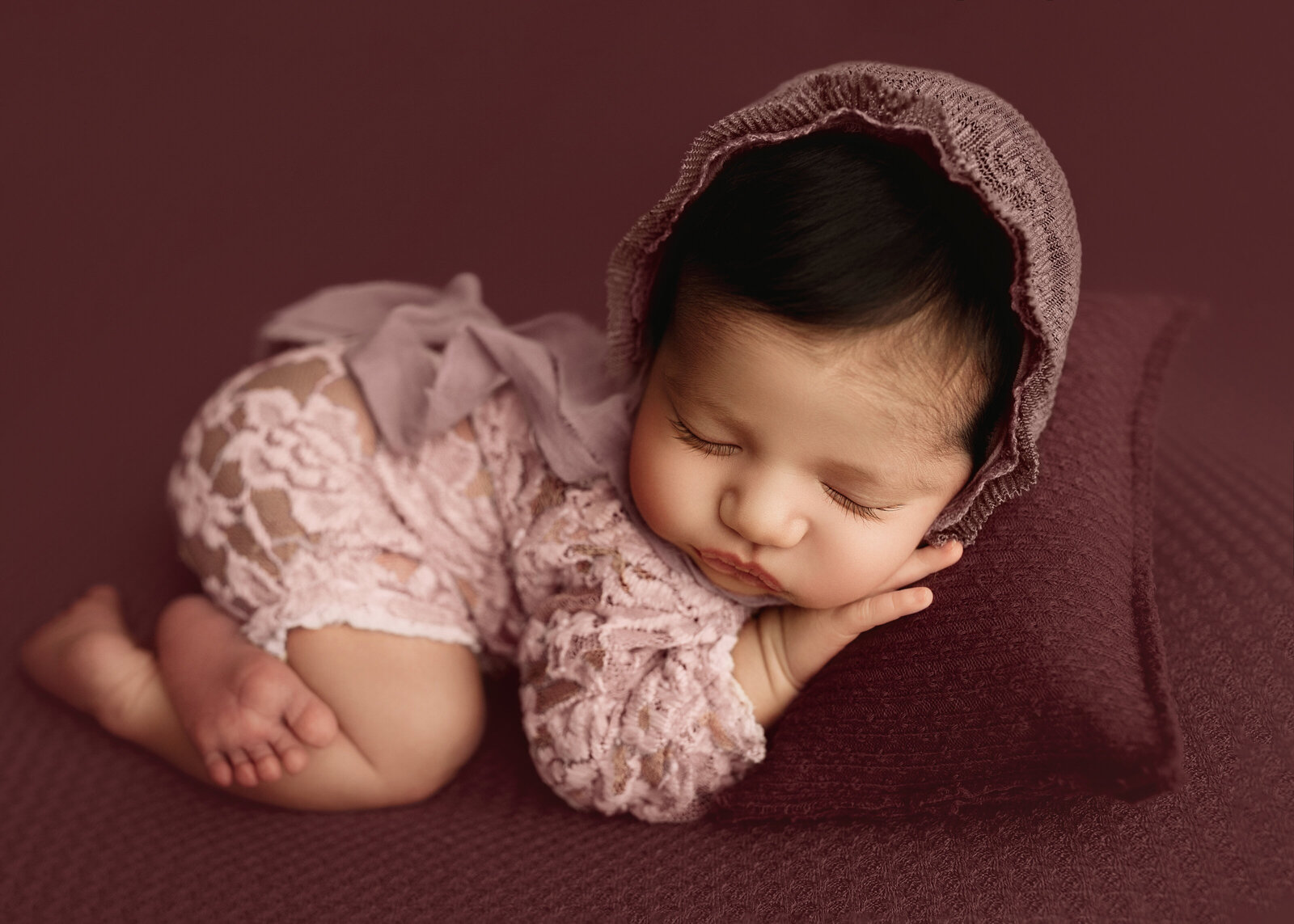 newborn baby wearing little outfit in pink mauve studio setting portrait