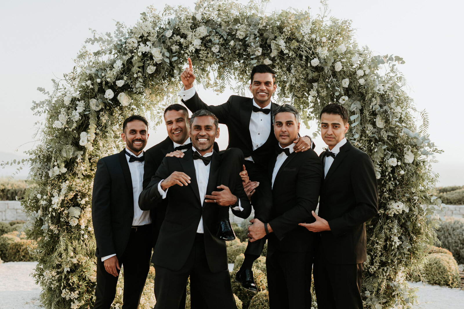 Groomsmen lifting groom up in Greece