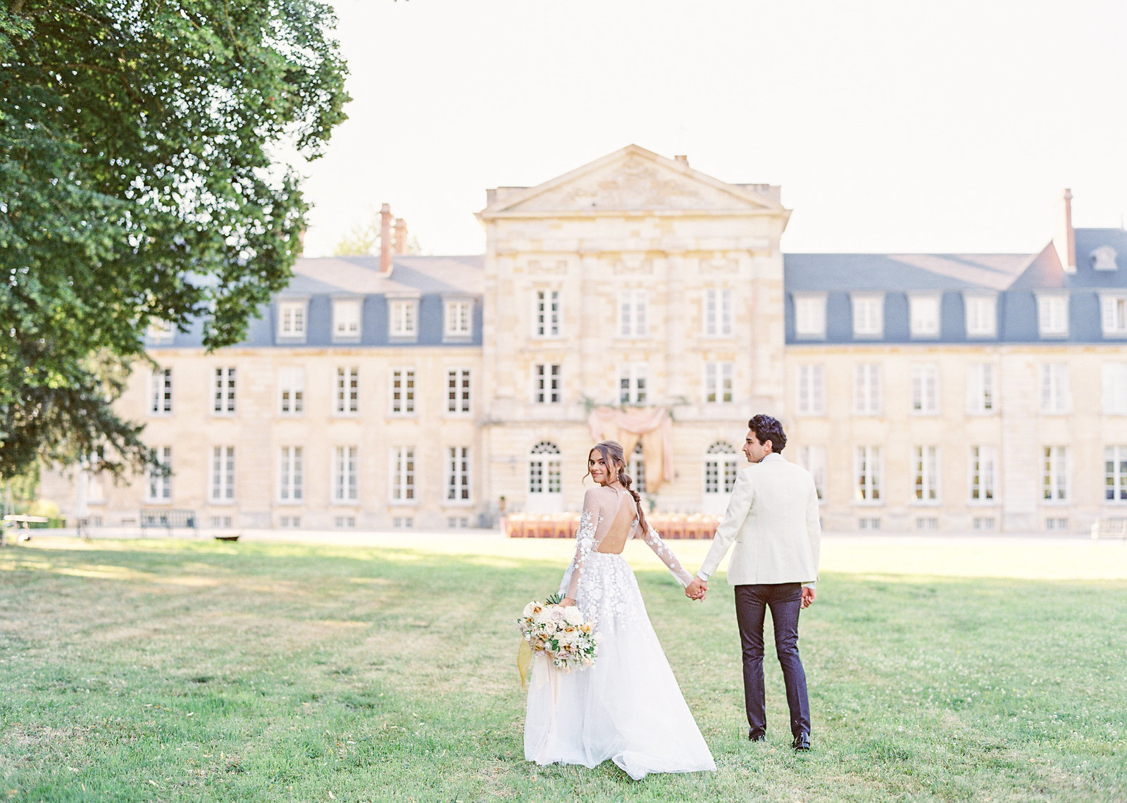 Bride and groom holding hands walking towards french chateau. Photographed by Amy Mulder Photography