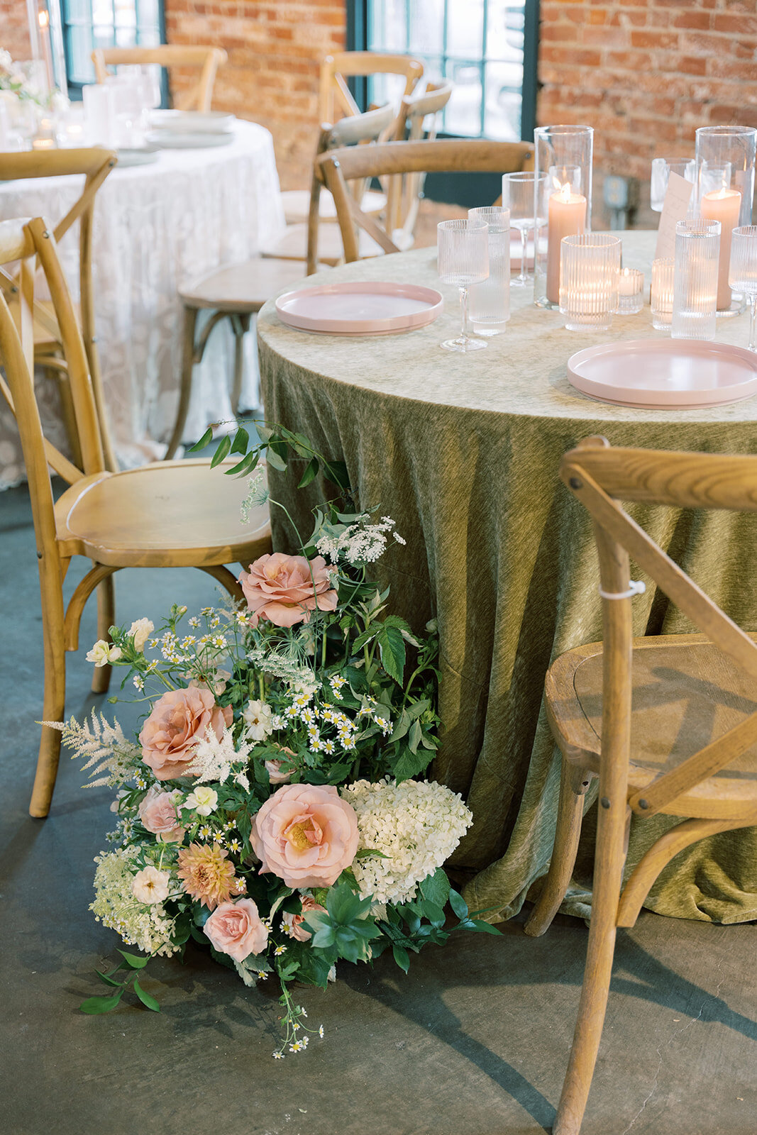 Round table at reception in the Washington mill dye house with floral ground arrangement beside a chair with peach and blush garden roses, white hydrangea, daisies, white astilbe, and queen anns lace and peach dahlias.