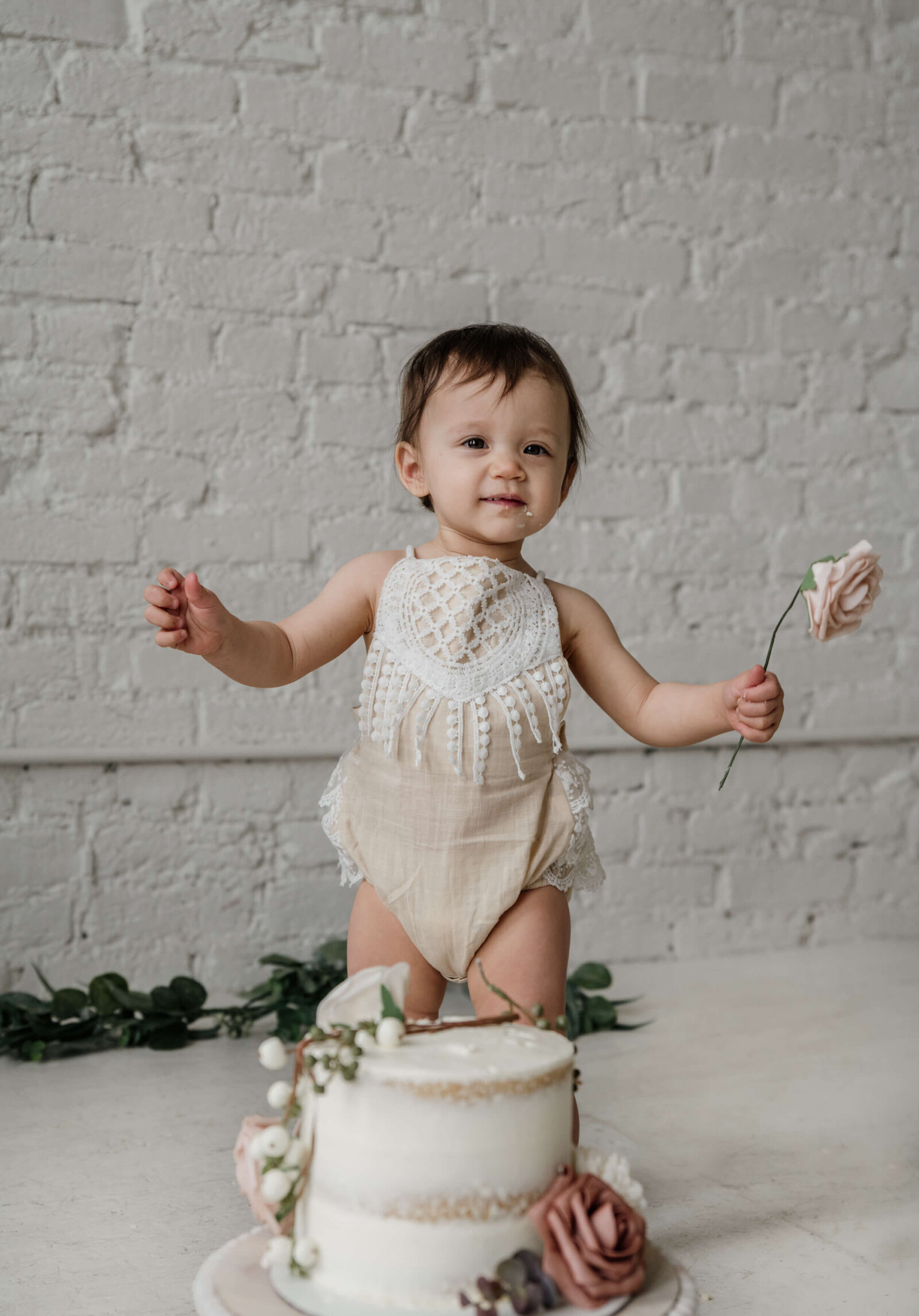 Baby girl holding flower behind her cake.