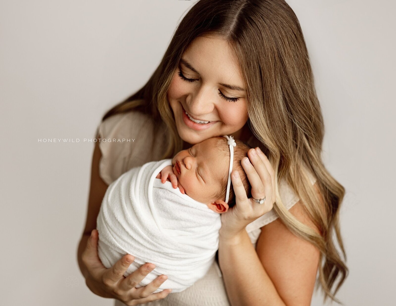 Smiling mother cradling her swaddled newborn baby during a luxury newborn session, photographed by Honeywild Photography in Grand Rapids, MI