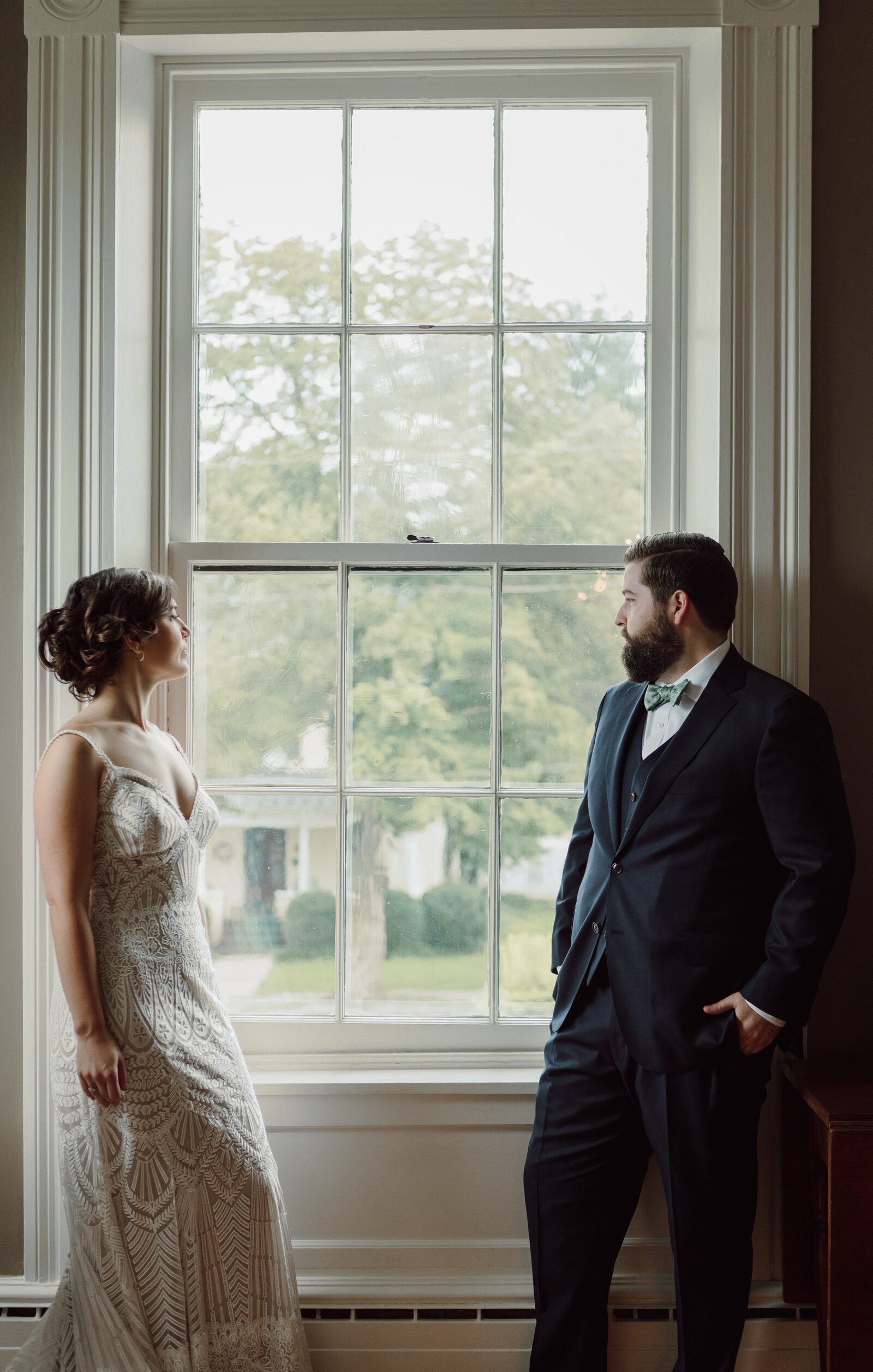 A bride and groom stand together looking out a window