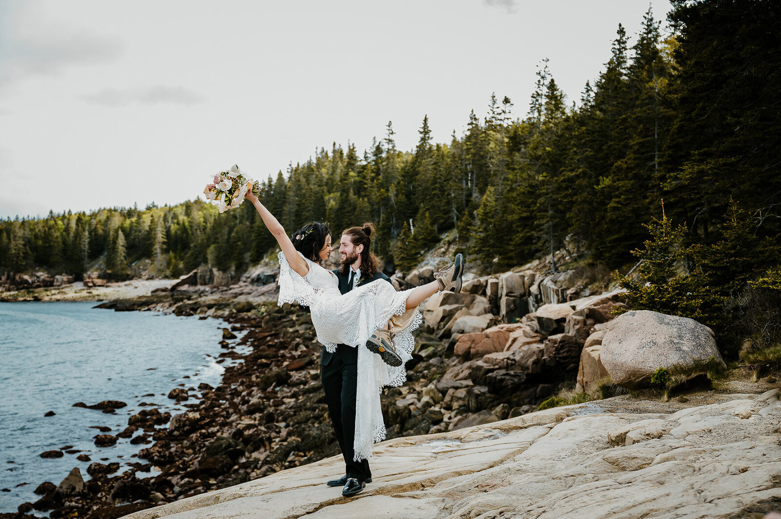 groom holds bride on shore