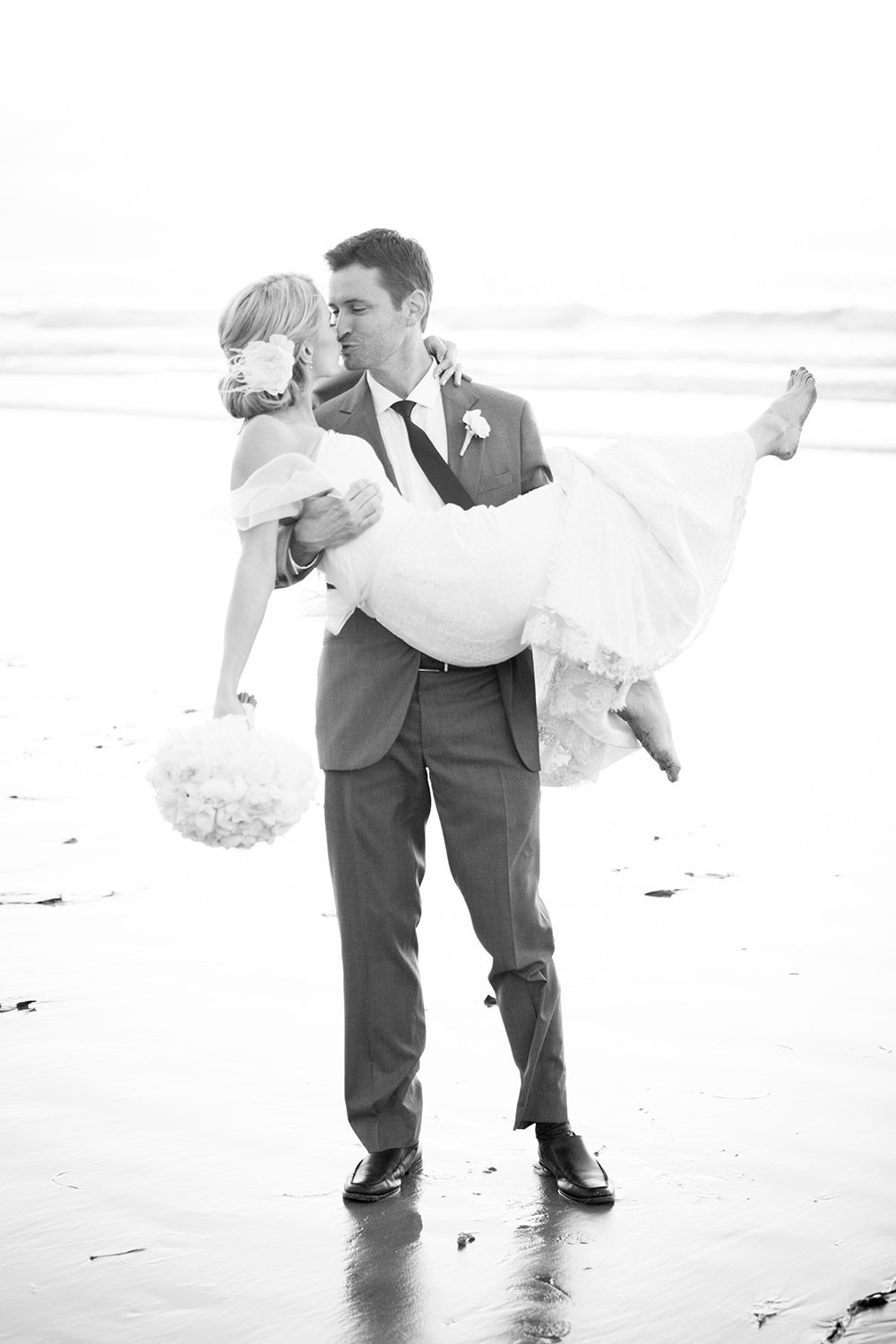 groom picking up bride on beach